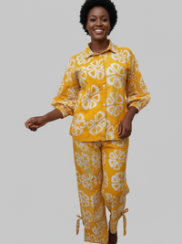 A person with short curly hair smiles while walking, wearing a yellow pajama set with white geometric patterns on a light gray background.