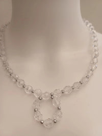 A clear bead necklace with a circular pendant design on a white mannequin bust. The necklace features faceted beads with small silver spacer beads.
