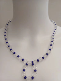 A transparent mannequin displays a beaded necklace made of clear and blue beads. The necklace forms a loop pendant at the front.