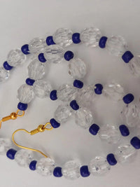 A necklace and earring set featuring clear faceted beads and small dark blue beads, with gold hooks and chain on a white background.