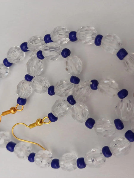 A necklace and earring set featuring clear faceted beads and small dark blue beads, with gold hooks and chain on a white background.
