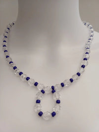 A necklace made of clear faceted beads interspersed with smaller dark blue beads, displayed on a white mannequin bust. The design features a loop at the center.