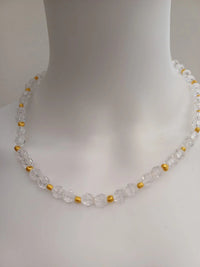 A clear beaded necklace with faceted beads interspersed with small gold spacers, displayed on a white mannequin bust.