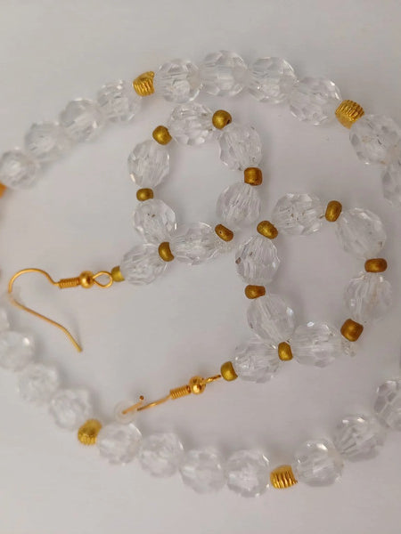 A necklace and matching earrings made of faceted clear beads and small gold beads, arranged on a white surface. The necklace features a gold clasp.