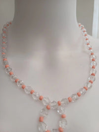 A close-up of a necklace on a mannequin. The necklace features clear faceted beads with small pink round beads between them.