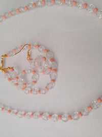 A beaded jewelry set with a necklace and earrings, featuring clear and pink beads. The necklace has a gold chain, and the earrings have gold hooks.