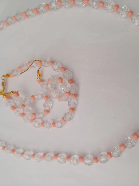 A beaded jewelry set with a necklace and earrings, featuring clear and pink beads. The necklace has a gold chain, and the earrings have gold hooks.