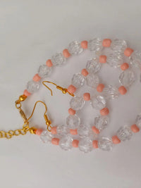 Gold chain and earrings with clear faceted beads and pink round spacers, arranged on a white background.