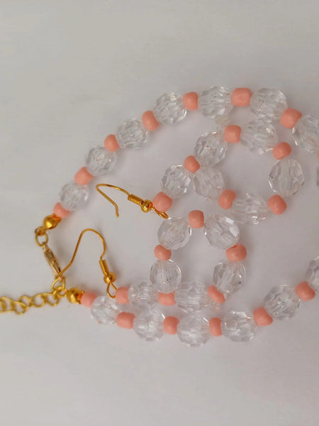 Gold chain and earrings with clear faceted beads and pink round spacers, arranged on a white background.