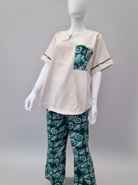 A mannequin wearing a cream-colored short-sleeve top with a dark green patterned pocket and trim, paired with matching green patterned pants.
