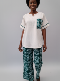 A woman with short curly hair smiles while wearing a white top with green patterned accents and matching green patterned pants.