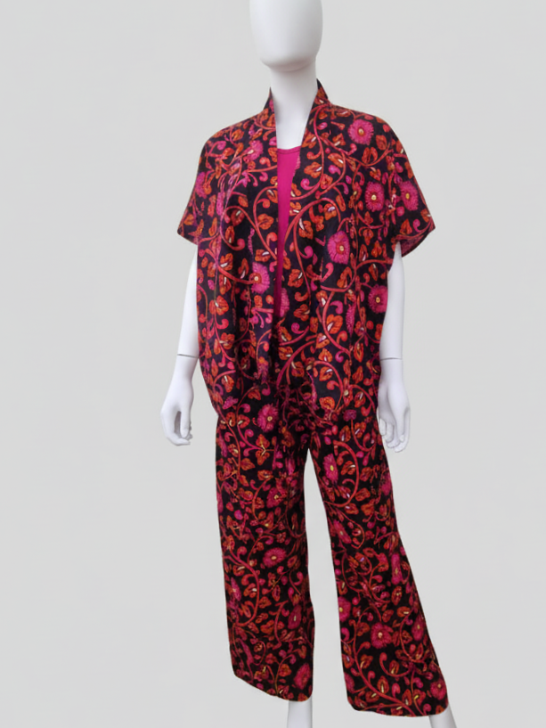 Mannequin wearing a matching set of loose-fitting pants and a short-sleeved jacket with a vibrant pink and orange floral pattern on a black background.