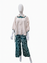 A mannequin wearing a beige blouse with teal patterned collar and cuffs, paired with teal patterned wide-leg pants.