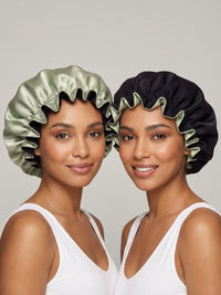 Two people wearing satin bonnets, one in green and black, the other in black and green, both in white tank tops, smiling.