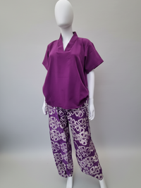 A mannequin wearing a purple tunic with short sleeves and patterned purple pants featuring white geometric designs, set against a plain background.