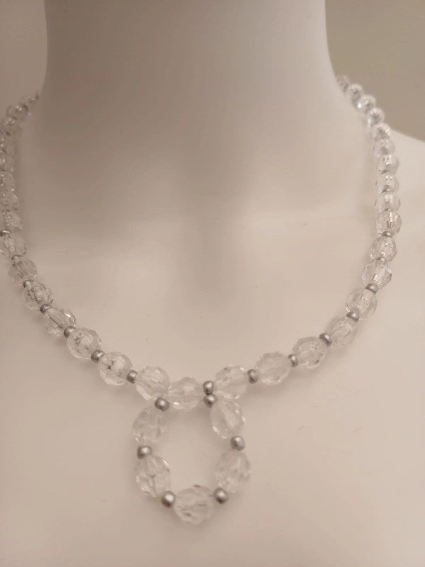 A clear beaded necklace with silver spacer beads, featuring a circular pendant design, displayed on a white mannequin bust.