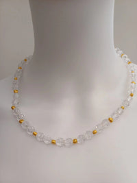A close-up of a beaded necklace displayed on a white mannequin bust. The necklace features clear, faceted beads interspersed with small gold spacers.