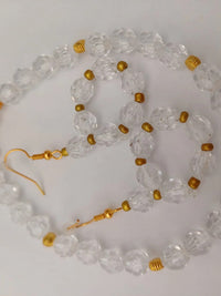 A necklace and matching earrings made of faceted clear beads and small gold beads, arranged on a white surface. The necklace features a gold clasp.
