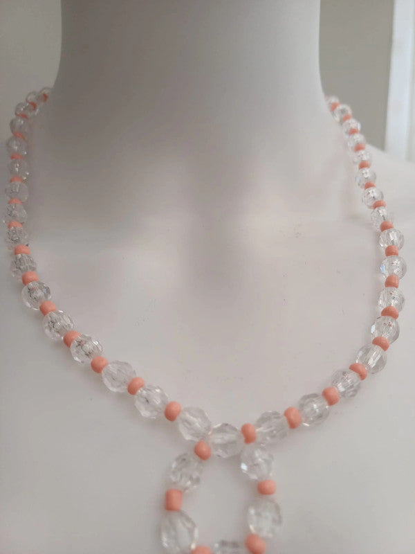 A close-up of a necklace on a mannequin. The necklace features clear faceted beads with small pink round beads between them.