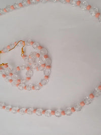 A necklace and earring set made of clear faceted beads and small pink beads, with gold-colored hooks and chain clasps, on a white background.