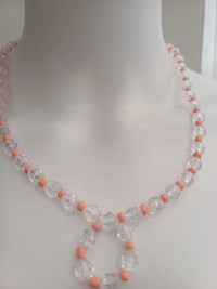 A clear and pink beaded necklace displayed on a white mannequin bust. The necklace features alternating transparent and pink beads.