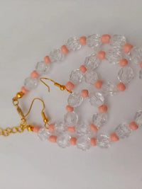 Gold chain and earrings with clear faceted beads and pink round beads, arranged on a white background.