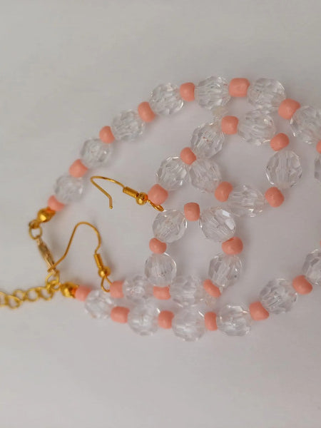 Gold chain and earrings with clear faceted beads and pink round beads, arranged on a white background.