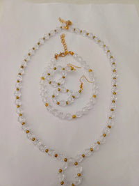 A jewelry set on a white background, featuring a clear bead necklace with gold accents, matching bracelet, and two earrings.