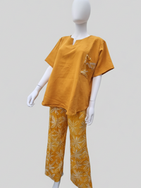 A mannequin wearing a mustard yellow top with a small patterned pocket and matching wide-leg pants featuring a floral design.