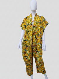 A white mannequin wearing a colorful outfit with a bold yellow, green, and black swirling pattern. The ensemble includes a short-sleeve shirt and matching pants.