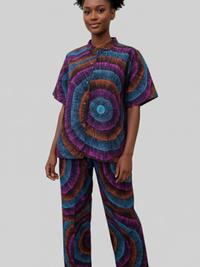 A person wearing a matching set with a vibrant circular pattern in blue, purple, and orange. The outfit includes a short-sleeved shirt and pants. The background is plain gray.