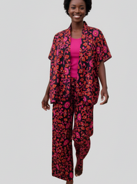 A person with short curly hair is walking barefoot, wearing a colorful floral outfit with a black background and pink accents over a matching pink top.