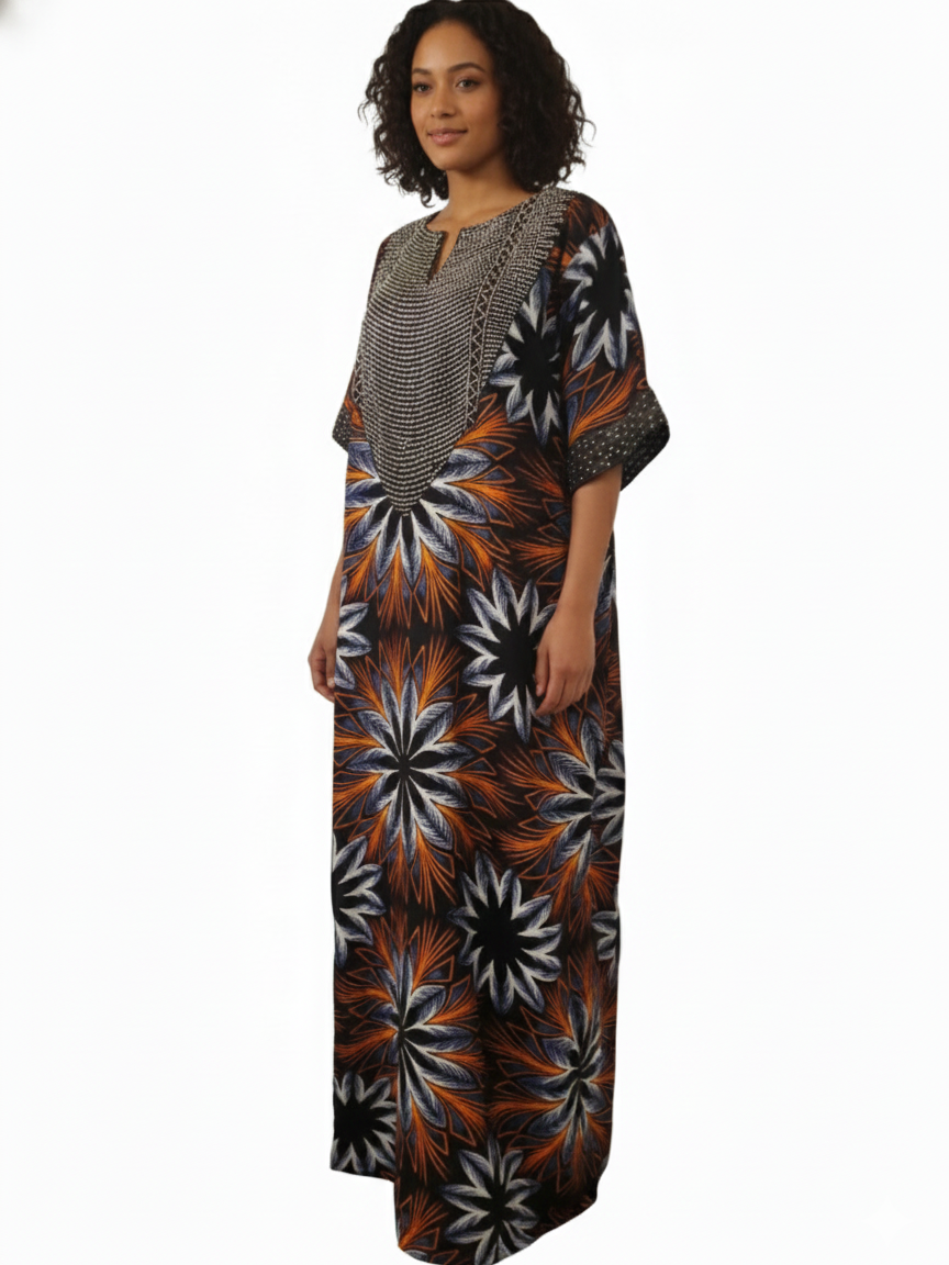 A woman models the Ankara Maxi Dress – Bold Sunburst Floral Print (Orange, Black & White) featuring a loose fit, patterned yoke, and short sleeves—perfect for cultural occasions—against a plain white background.