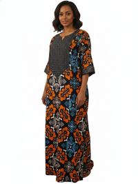 A woman with shoulder-length dark hair and a neutral expression wears the African Print Maxi Dress – Vibrant Floral Pattern, showcasing bold orange, blue, and black geometric and floral designs plus a black-and-white patterned chest panel.