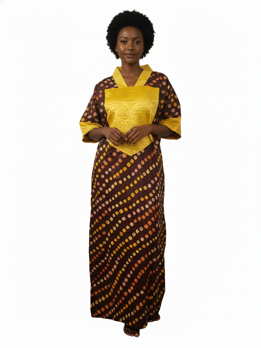 A woman stands barefoot in a Brown & Gold Ankara Kaftan Dress featuring a long, loose fit, yellow collar and sleeves, and a brown base with diagonal yellow, orange, and beige dotted patterns. The background is plain white.