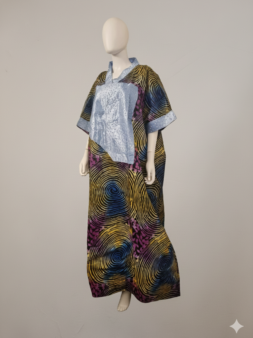 A mannequin displays the Ankara Maxi Kaftan Dress – Multi-Color Swirl Pattern with Light Blue Accent, a loose-fit maxi with wide sleeves and bold yellow, purple, and blue spirals, set against a plain beige background.