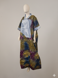 A mannequin displays the Ankara Maxi Kaftan Dress – Multi-Color Swirl Pattern with Light Blue Accent, a loose-fit maxi with wide sleeves and bold yellow, purple, and blue spirals, set against a plain beige background.