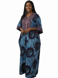 A woman with long braided hair smiles, wearing the Elegant Blue & Purple Ankara Kaftan Dress with floral patterns, posing against a white background.