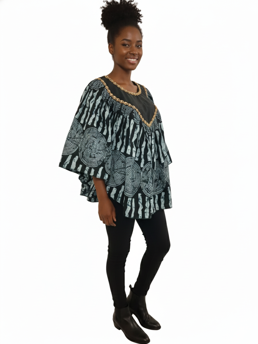 A smiling woman stands against a white background, wearing the Black & Mint Green Ankara Batik Poncho Top with black leggings and boots. Her hair is styled in a high puff.
