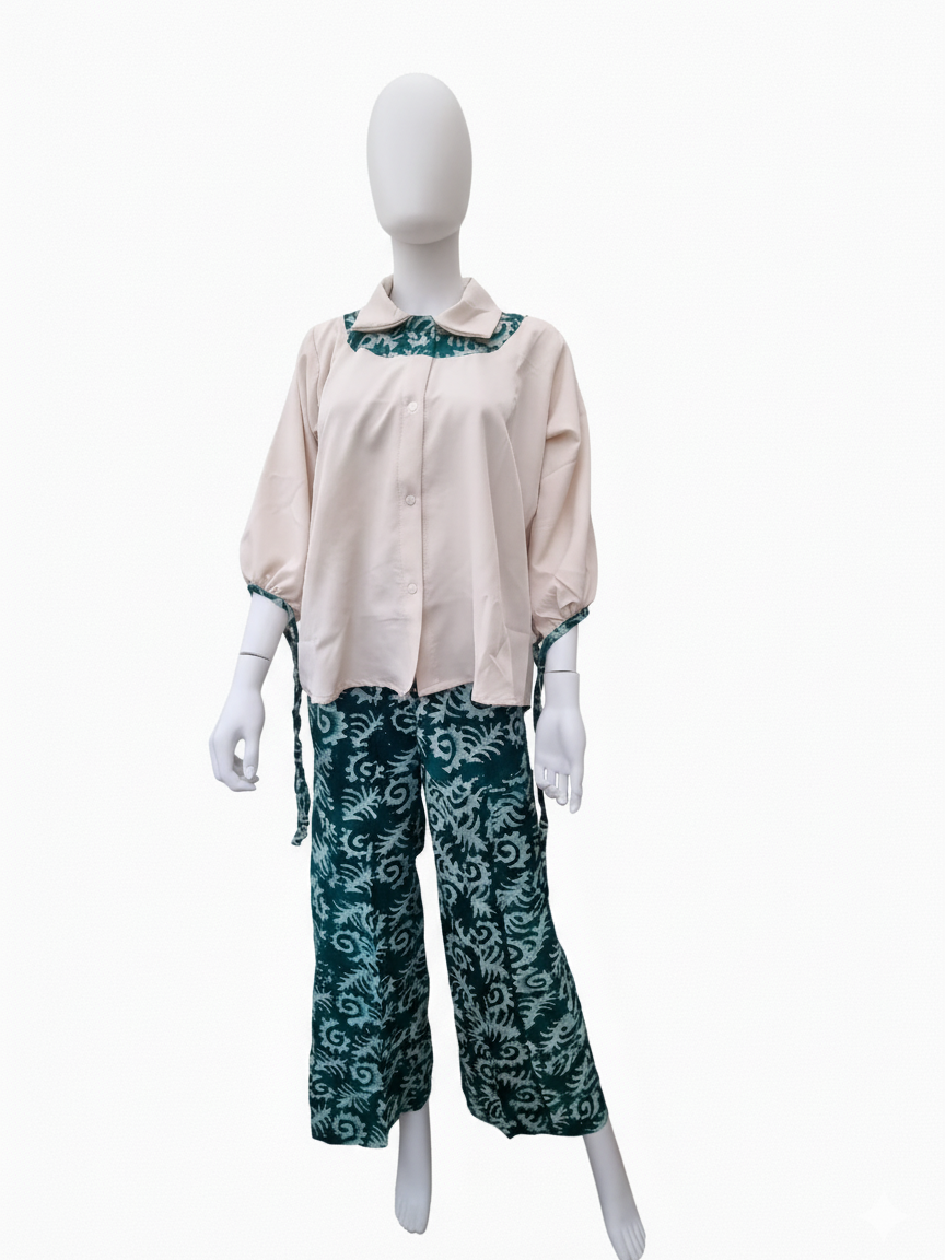 A mannequin wearing a beige blouse with teal patterned collar and cuffs, paired with teal patterned wide-leg pants.