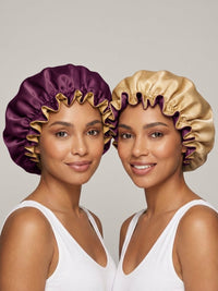 Two women wearing satin bonnets, one in purple with gold trim and the other in gold with purple trim, both in white tank tops.