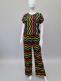 A mannequin wearing a zigzag-patterned outfit with vibrant colors including purple, green, orange, and yellow on a light gray background.