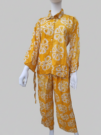 A mannequin wearing a yellow button-up shirt and pants with a white geometric pattern, set against a plain background.