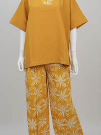 Mannequin wearing a mustard yellow top with a wide collar and matching pants featuring a white floral pattern. A sign reads "Kampala Style Comfort Set."